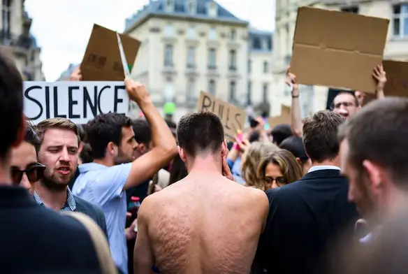 En gruppe demonstranter i Brussels europeiske kvartal, deriblant en mann uten skjorte, holder plakater med teksten SILENCE og andre slagord under en protest mot den midlertidige stillhetssonen.
